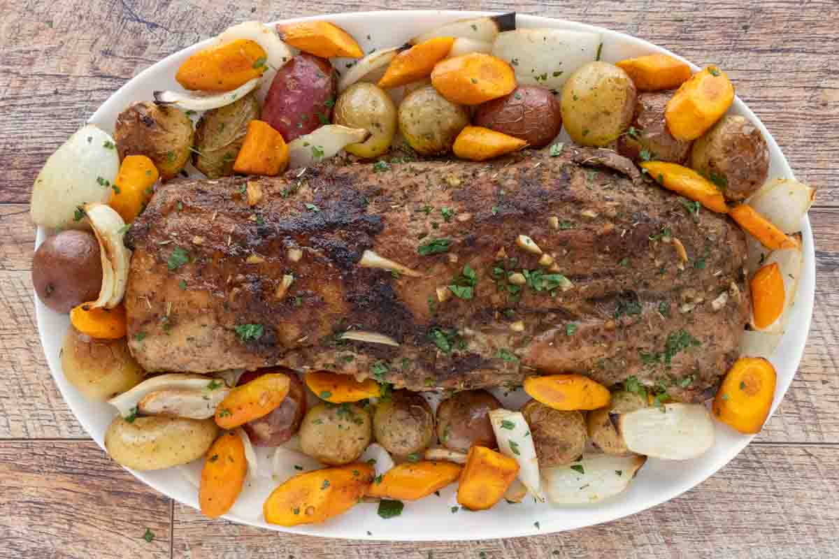 Roasted pork loin with. vegetables on a white platter.