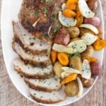 Sliced roasted pork loin with vegetables on a white platter.