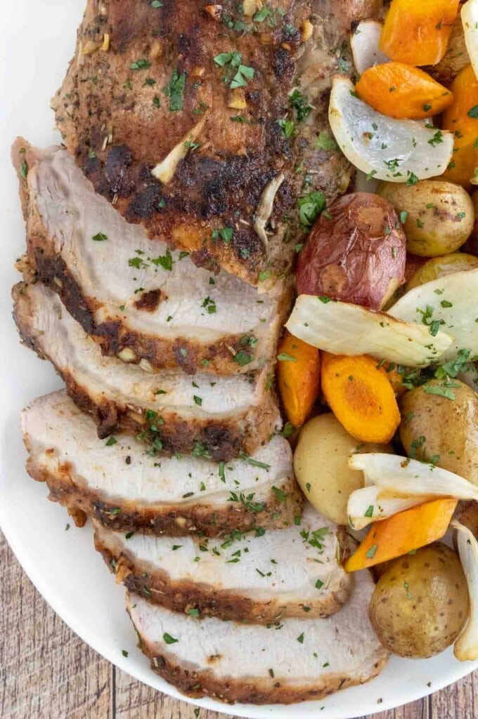 Sliced roasted pork loin with vegetables on a white platter.