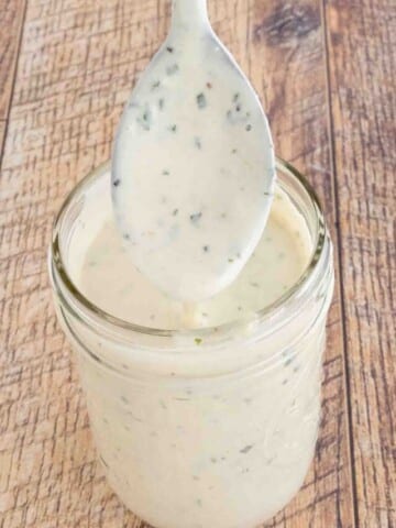 Garlic parmesan sauce in a glass jar with a spoon coming out.