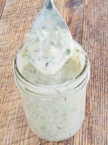 Raita sauce in a glass jar with a spoon coming out.