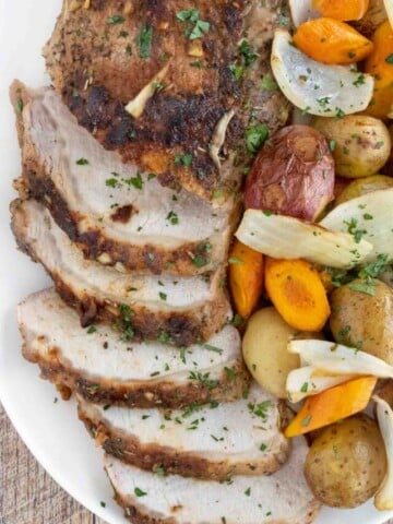 Sliced roasted pork loin with vegetables on a white platter.