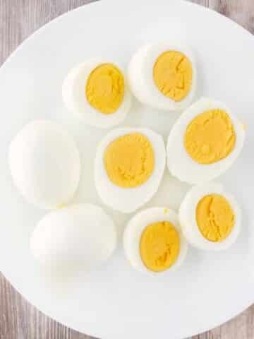 Two hard cooked eggs next to eggs sliced in half on a white plate.