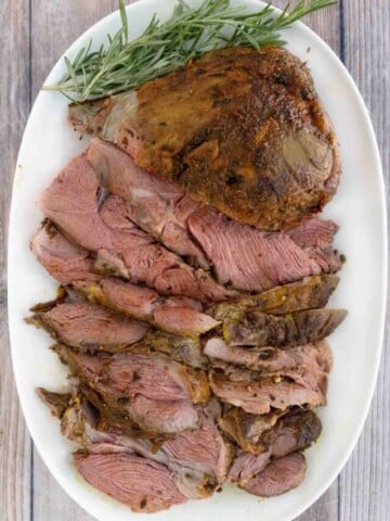 Smoked leg of lamb roast with sliced lamb on a white platter.