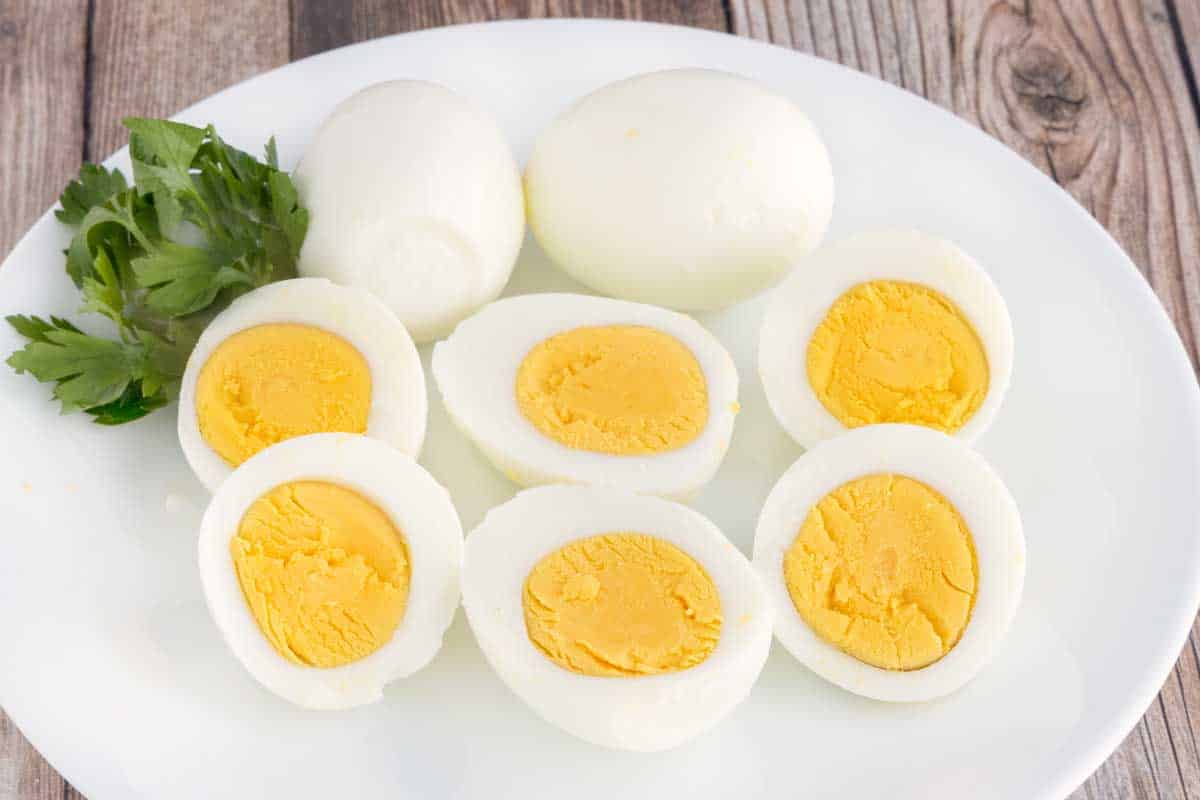 Two hard-boiled eggs next to eggs sliced in half on a white plate.