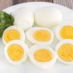 Two hard cooked eggs next to eggs sliced in half on a white plate.