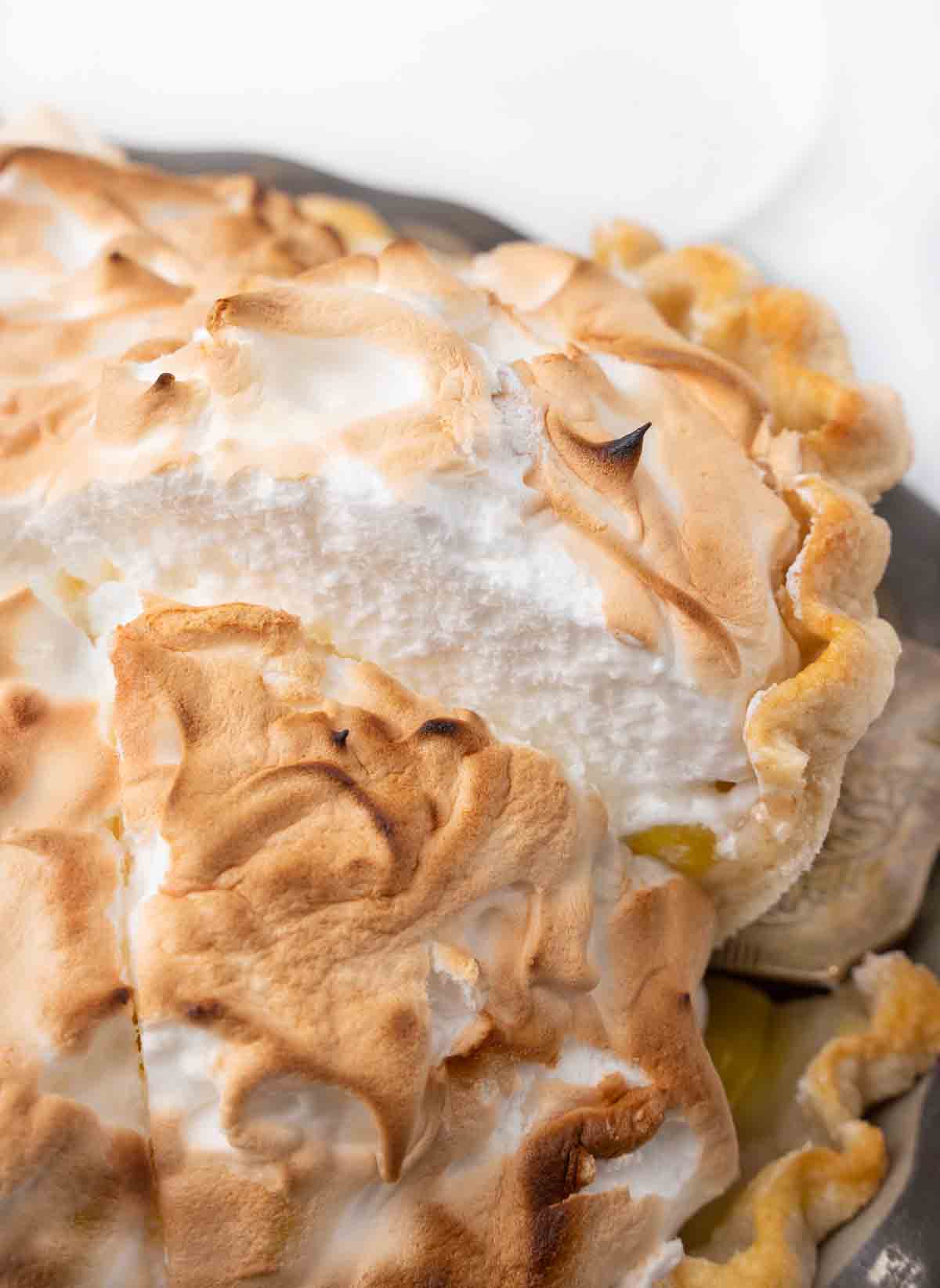 Slice of lemon meringue pie being taken out of the whole pie.