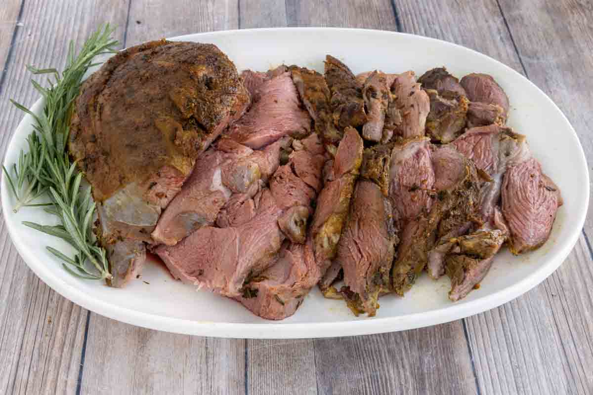 Smoked leg of lamb roast with sliced lamb on a white platter.