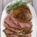 Smoked leg of lamb roast with sliced lamb on a white platter.