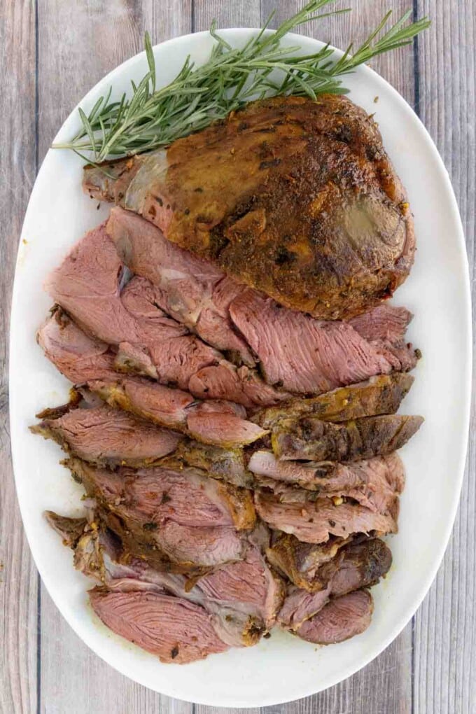 Smoked leg of lamb roast with sliced lamb on a white platter.