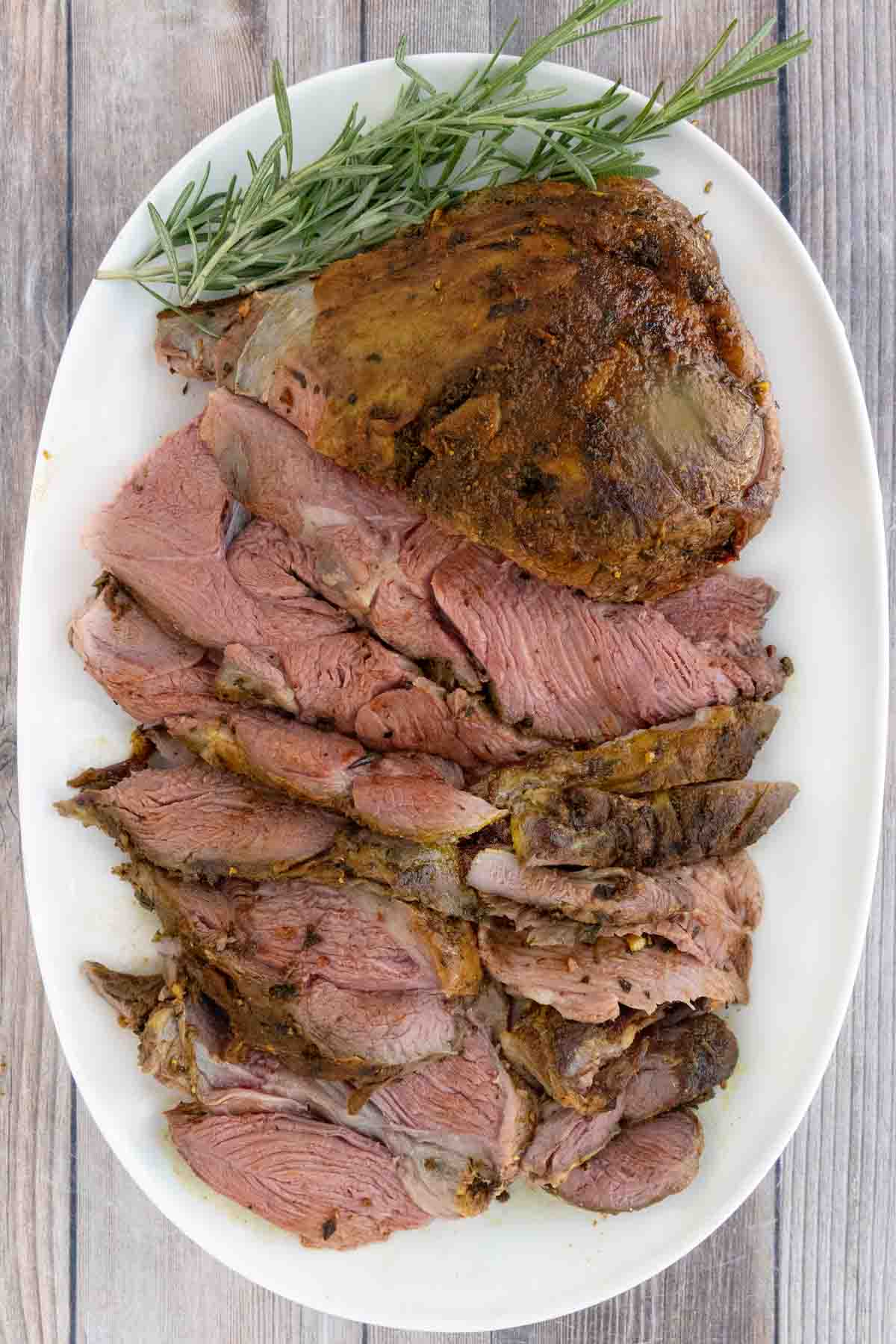 Smoked leg of lamb roast with sliced lamb on a white platter.