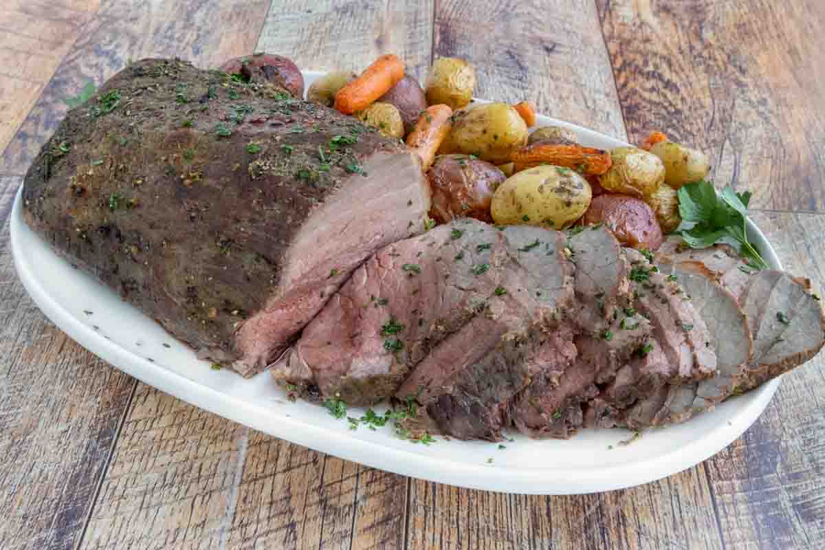 Sliced eye round of roast with potatoes and carrots on a white platter.