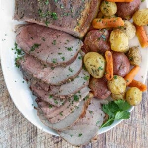 Sliced eye round of roast with potatoes and carrots on a white platter.