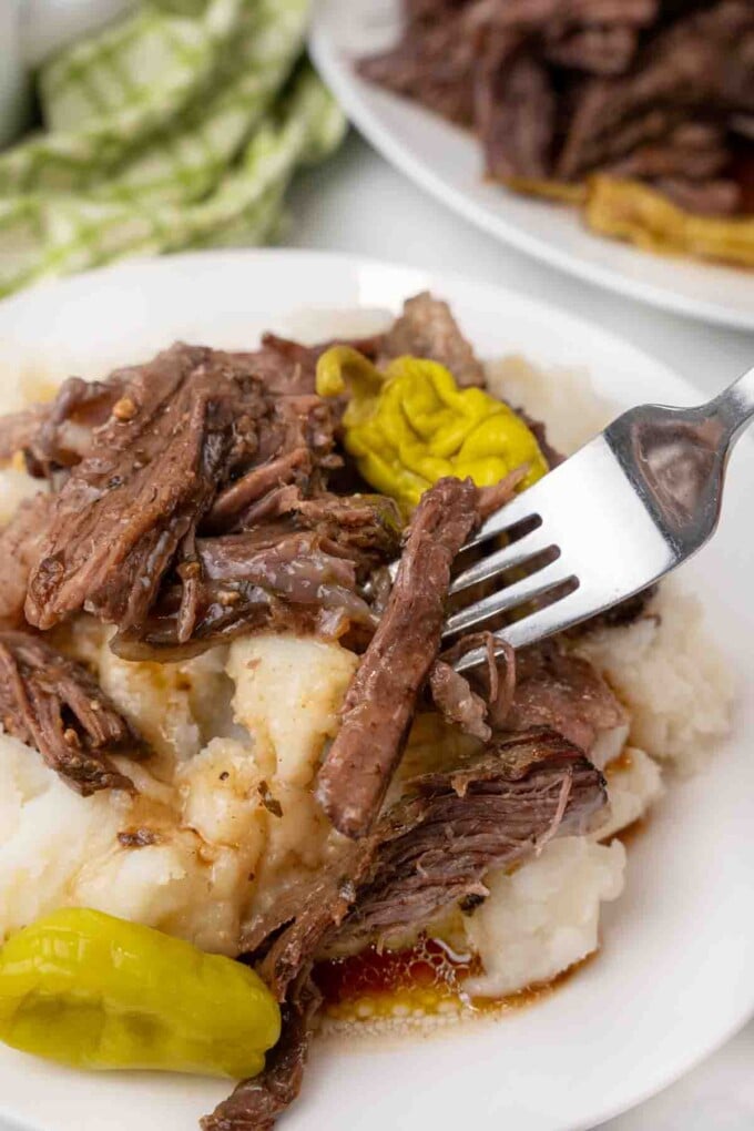 Shredded MIssissippi pot roast on a white plate with a fork.