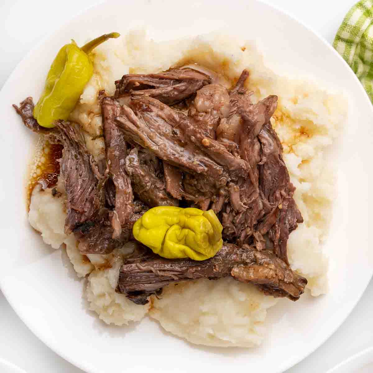 Shredded MIssissippi pot roast on a bed of mashed potatoes on a white plate.