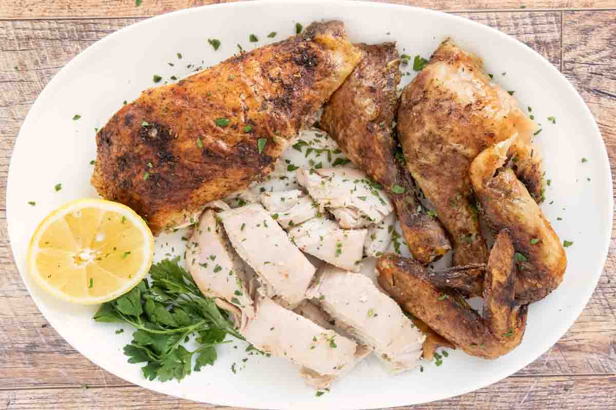 Herb roasted picture cut into pieces on a white platter with a lemon half and parsley.