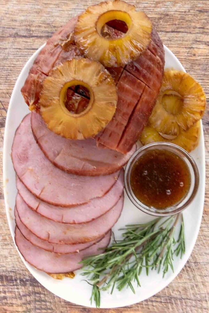 Smoked ham topped with pineapple with slices fanned out on a white platter.