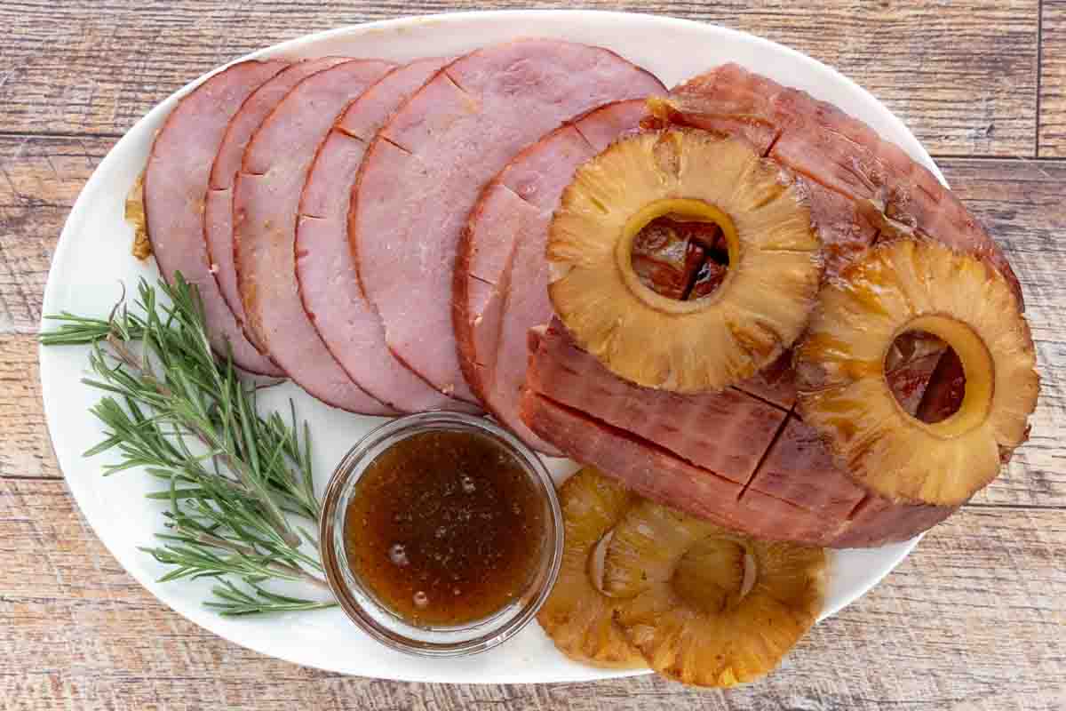 Smoked ham topped with pineapple with slices fanned out on a white platter.