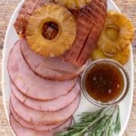 Smoked ham topped with pineapple with slices fanned out on a white platter.