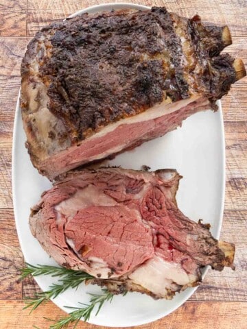 Slice of smoked prime rib on a white platter with the rest of the roast.