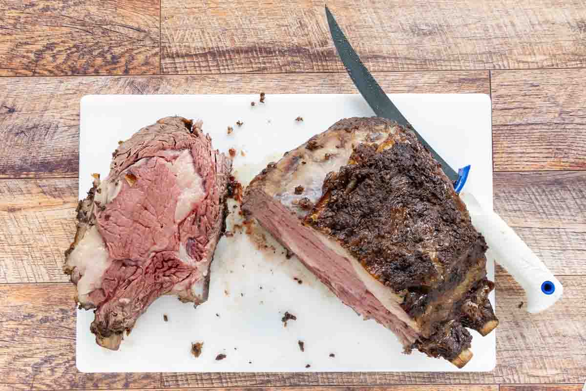 Prime rib on cutting board with one slice next to the roast and a knife.