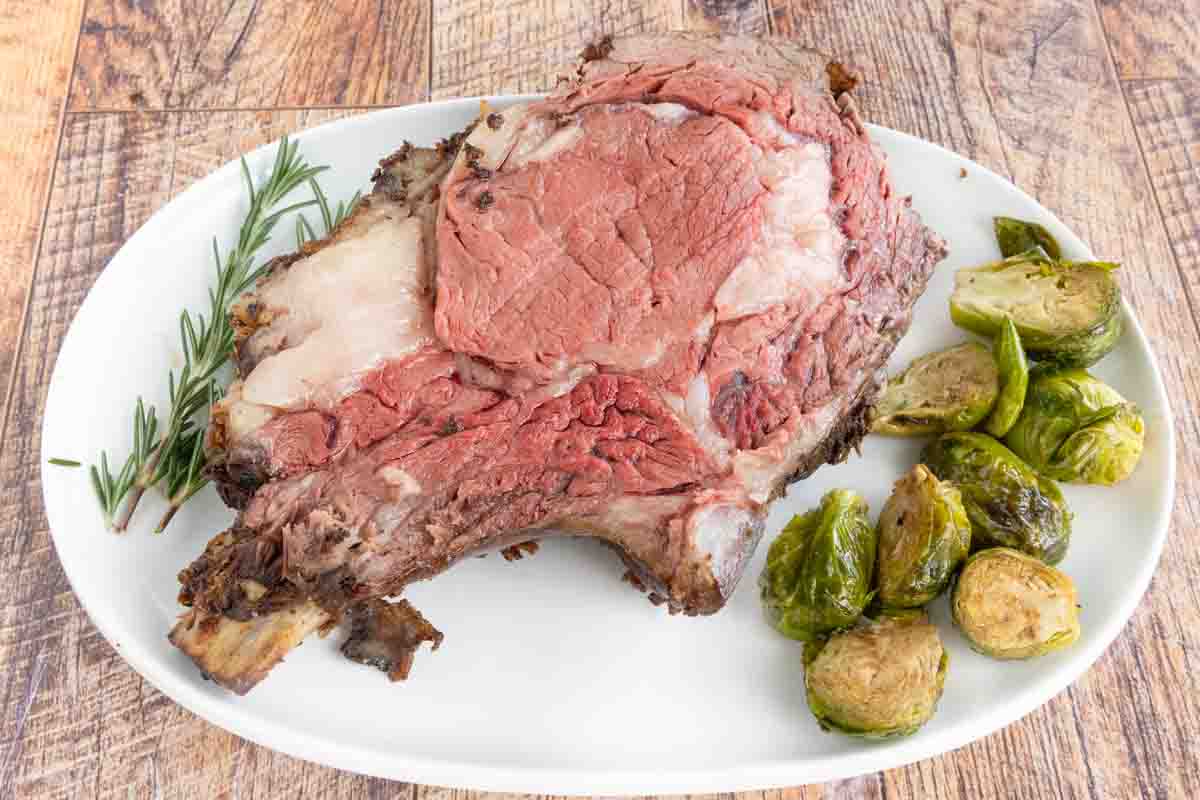 Slice of smoked prime rib on a white platter with Brussels sprouts.