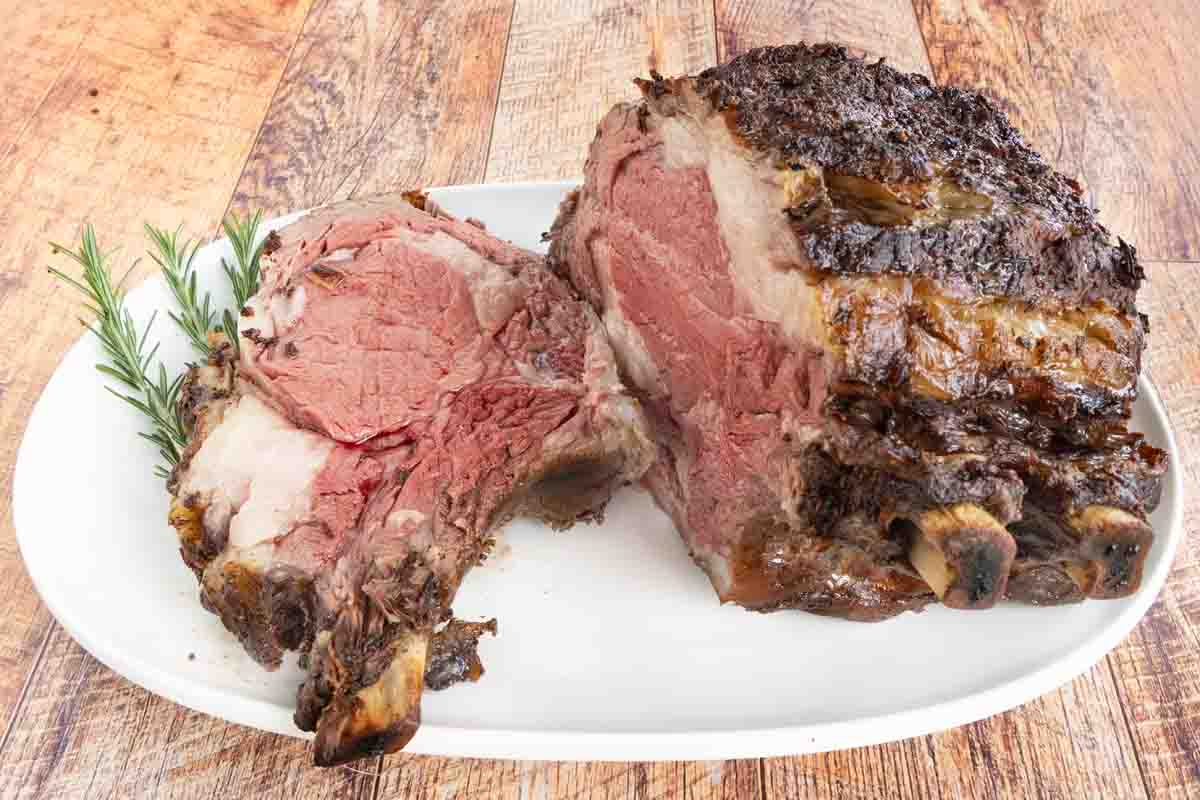 Slice of smoked prime rib on a white platter with the rest of the roast.