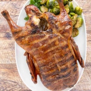 Whole smoked duck on a white platter with brussels sprouts.