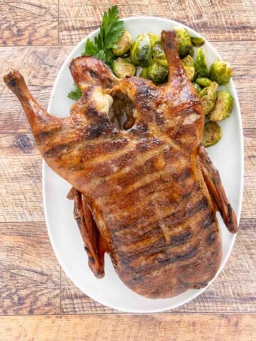 Whole smoked duck on a white platter with brussels sprouts.