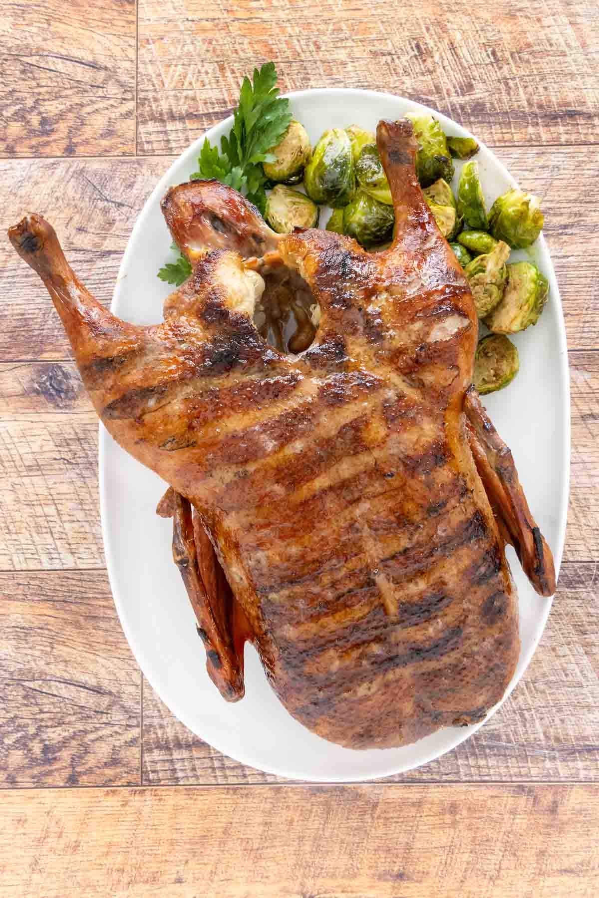 Whole smoked duck on a white platter with brussels sprouts.