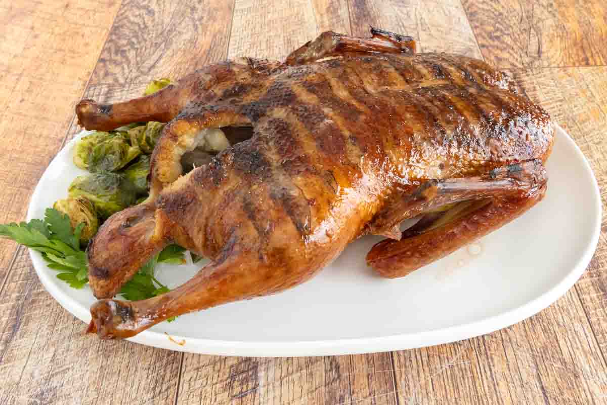 Whole smoked duck on a white platter with brussels sprouts.