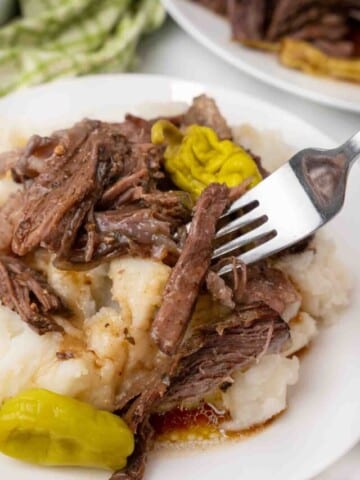 Shredded MIssissippi pot roast on a white plate with a fork.