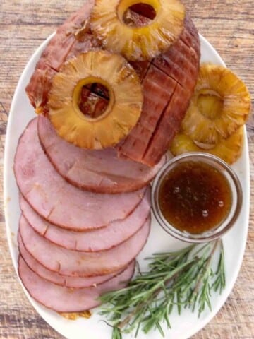 Smoked ham topped with pineapple with slices fanned out on a white platter.