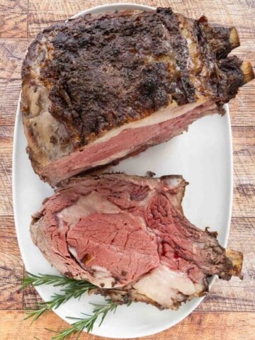 Slice of smoked prime rib on a white platter with the rest of the roast.