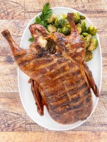 Whole smoked duck on a white platter with brussels sprouts.