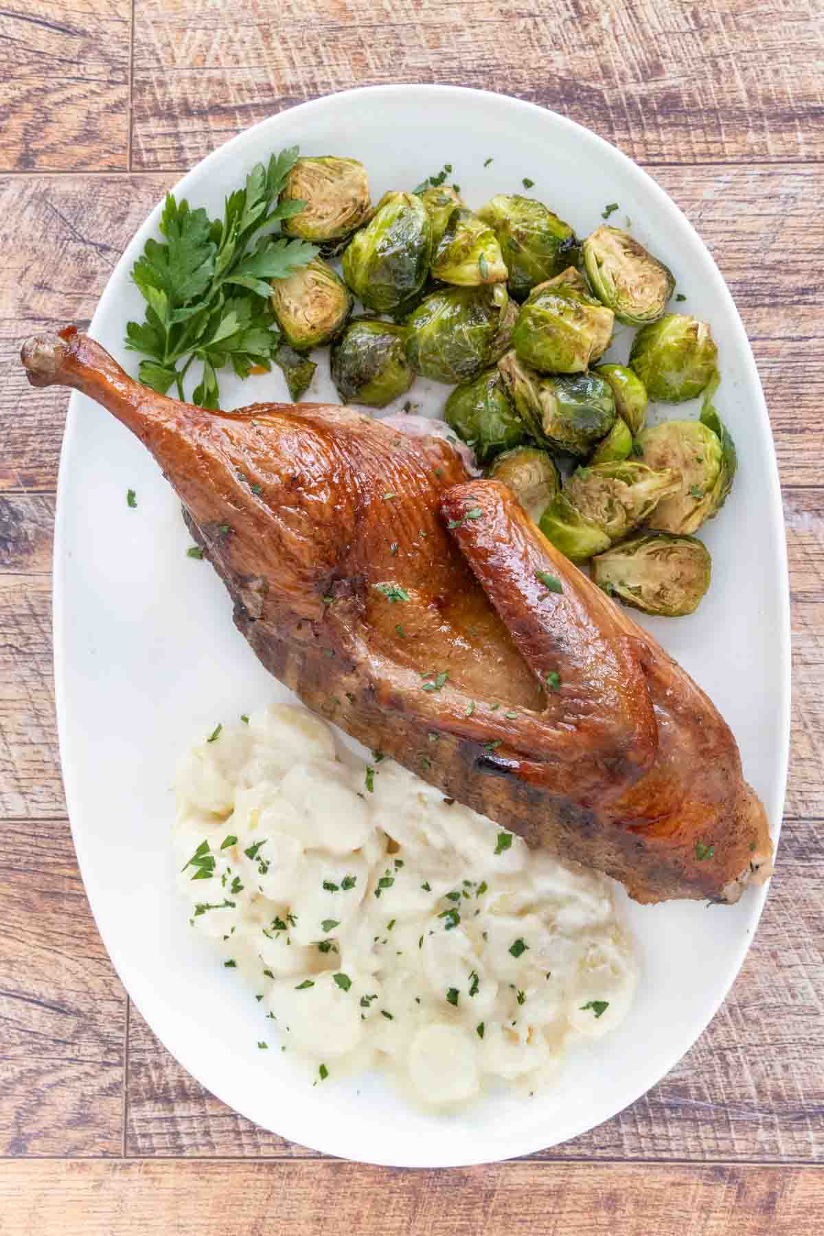 Half smoked duck with brussels sprout and gnocchi on a white plate.