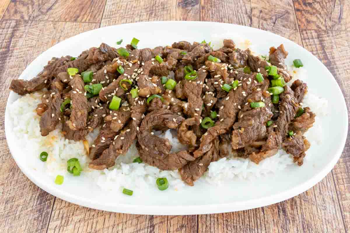 Beef Bulgogi on a bed of white rice on a white platter.