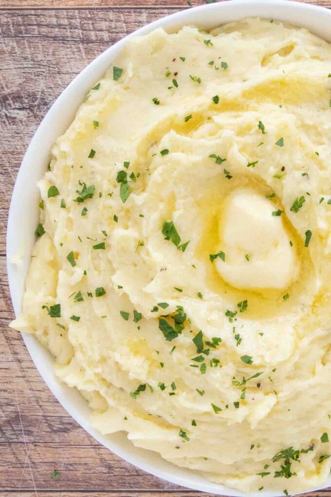 Cheesy mashed potatoes with a pat of melting butter in a white bowl.