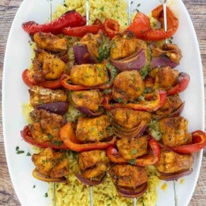 Skewered chicken kabobs on a bed of yellow rice on a white platter.