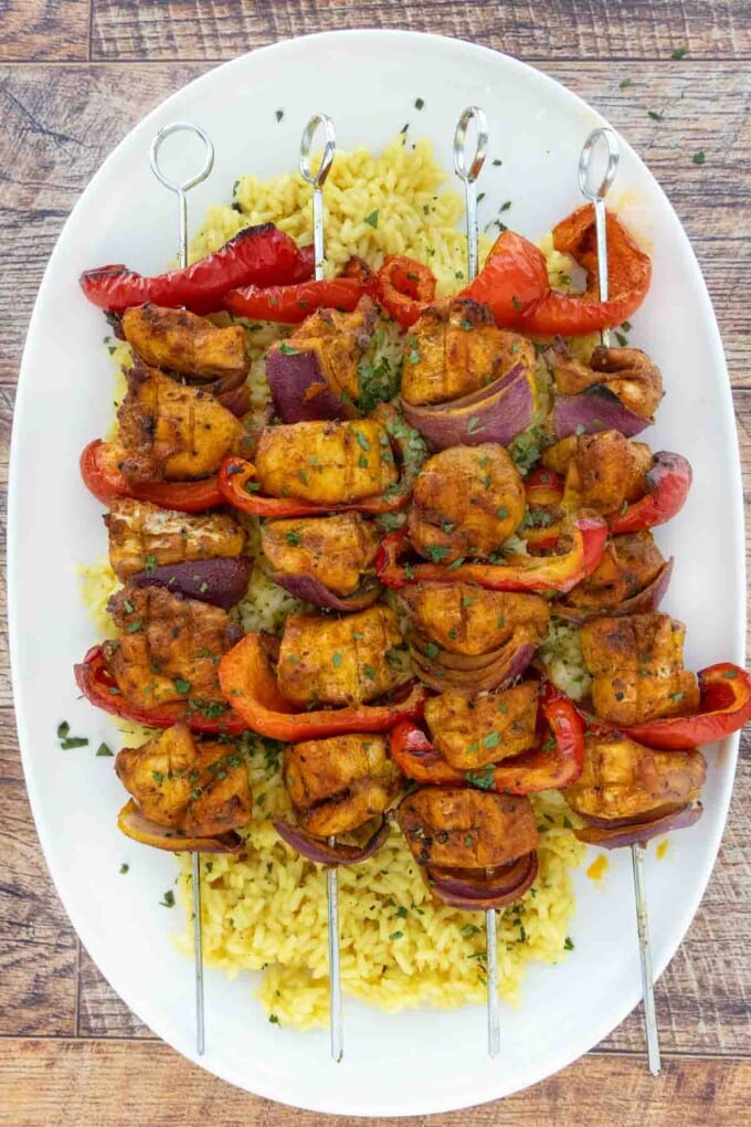 Skewered chicken kabobs on a bed of yellow rice on a white platter.