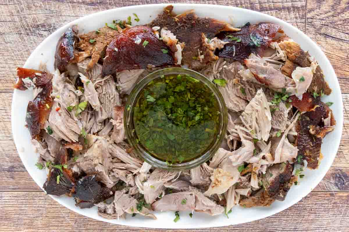 Pulled Pernil Pernil (Puerto rican Roasted Pork) on a white platter with green sauce.