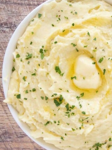 Cheesy mashed potatoes with a pat of melting butter in a white bowl.