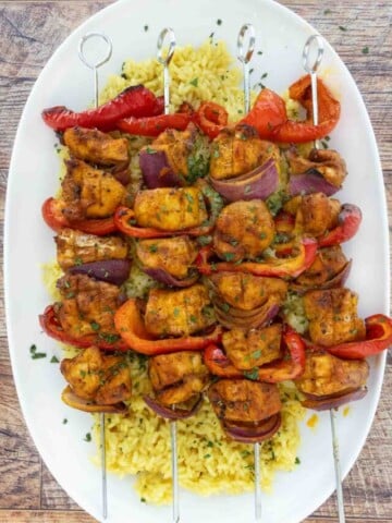 Skewered chicken kabobs on a bed of yellow rice on a white platter.