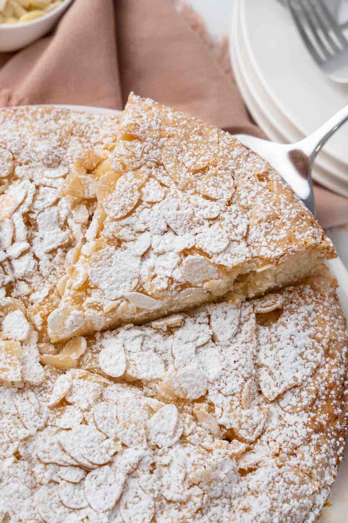 Slice of almond cake being taken out of the whole cake.