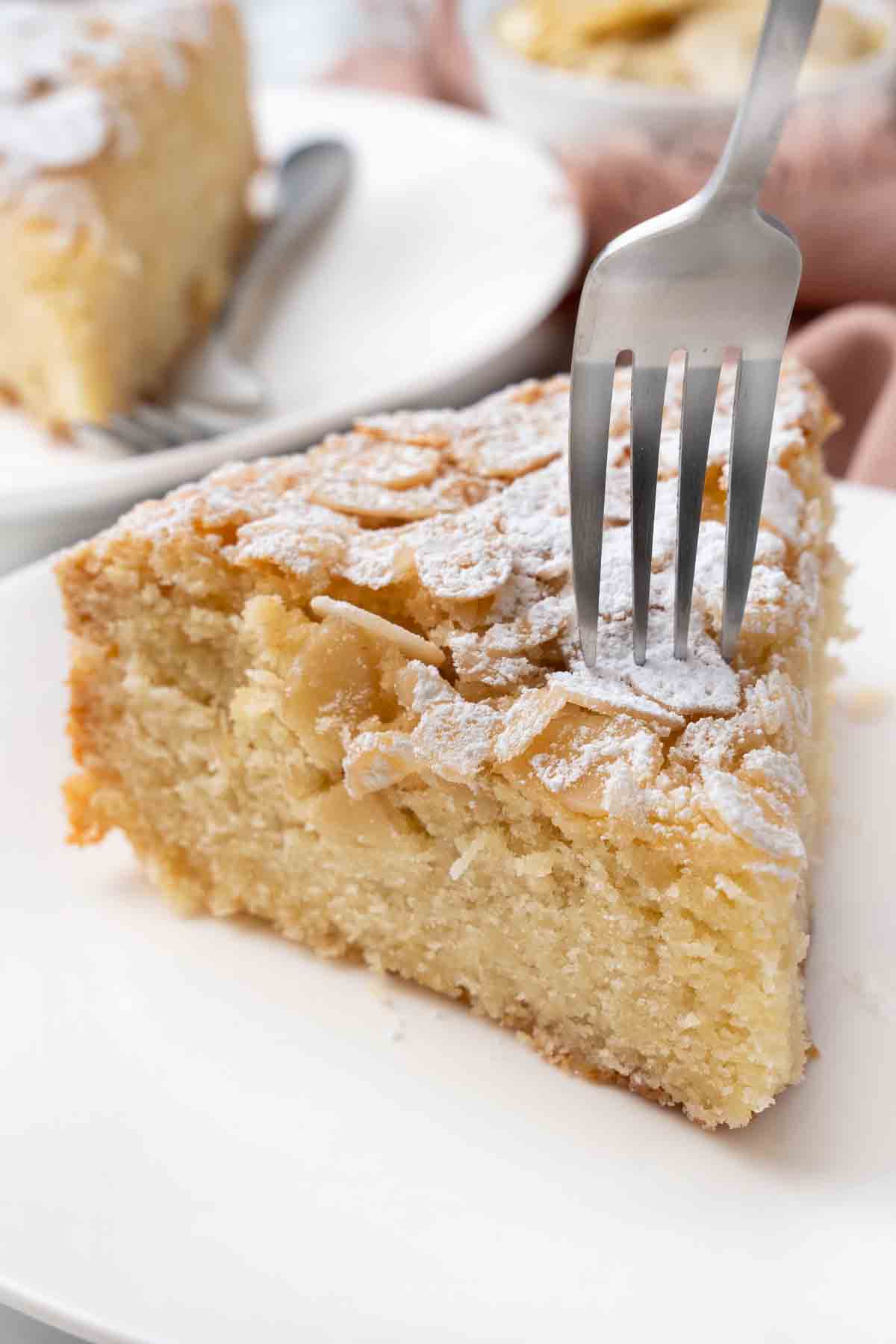 Slice of almond cake with a fork in it on a white plate.