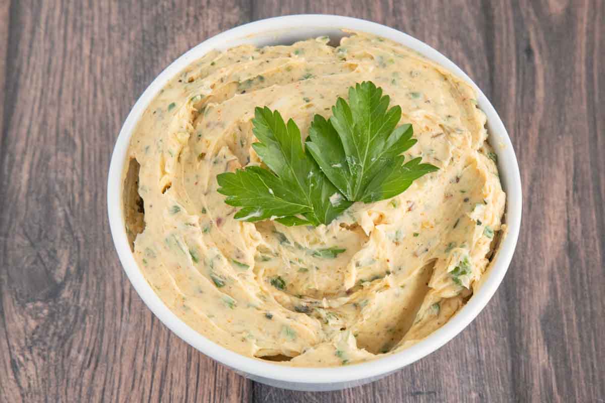 Cowboy butter in a white bowl with a sprig of parsley on top.