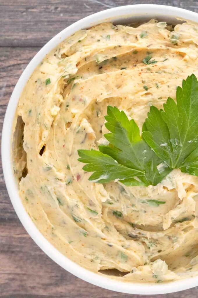 Cowboy butter in a white bowl with a sprig of parsley on top.