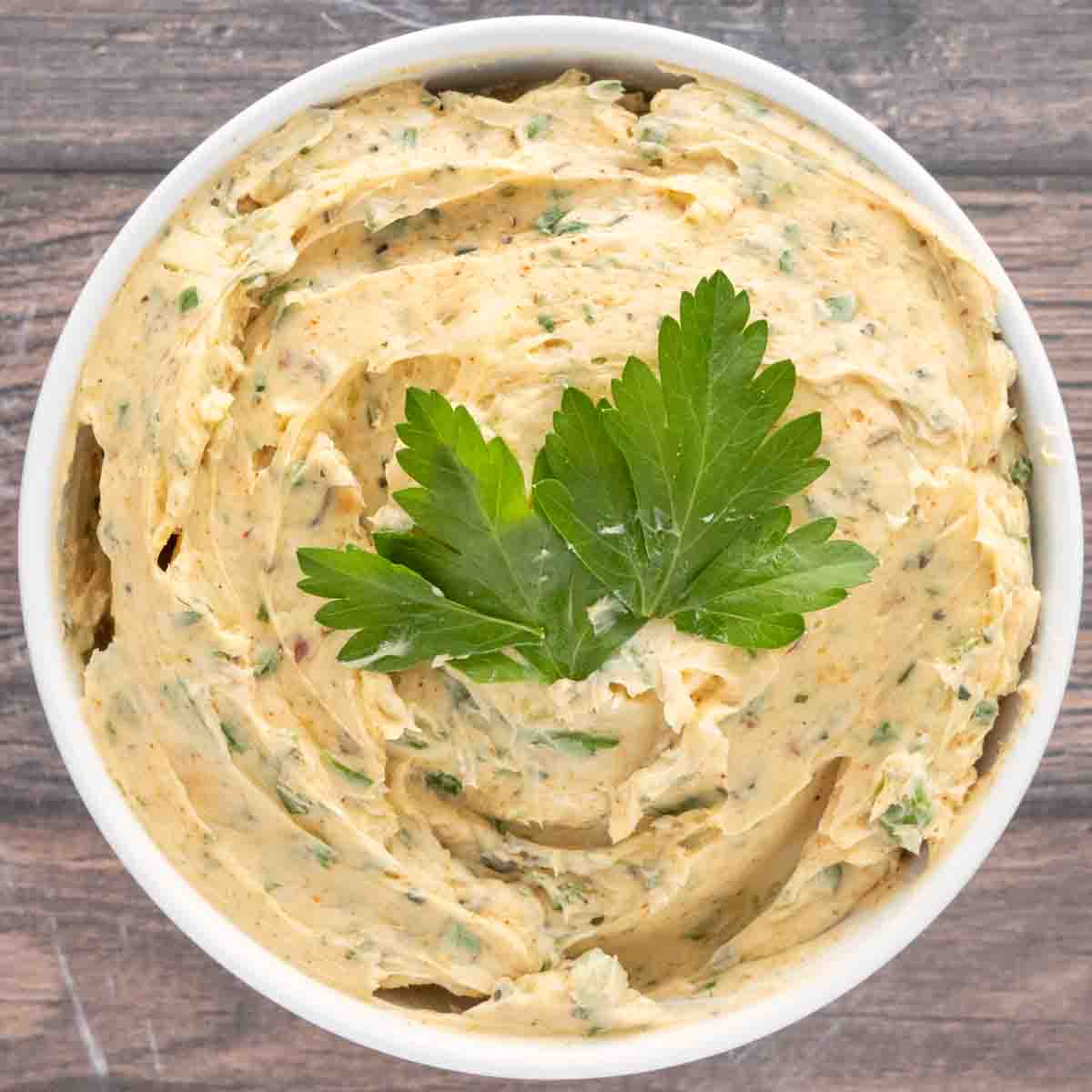 Cowboy butter in a white bowl with a sprig of parsley on top.