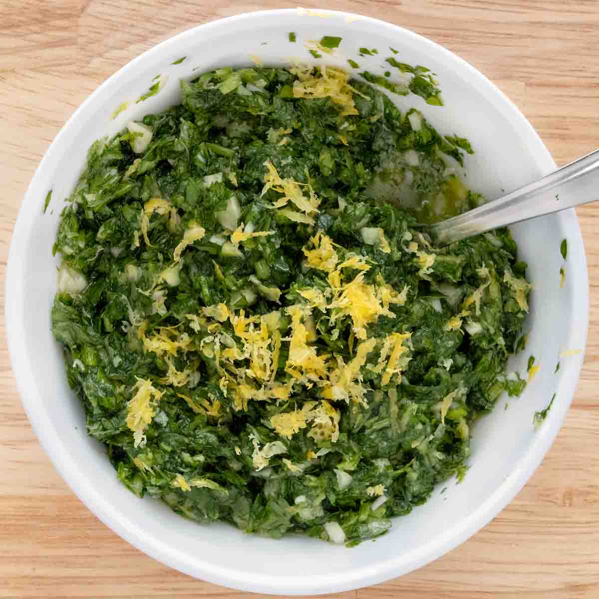 Gremolata in a white bowl with a spoon.