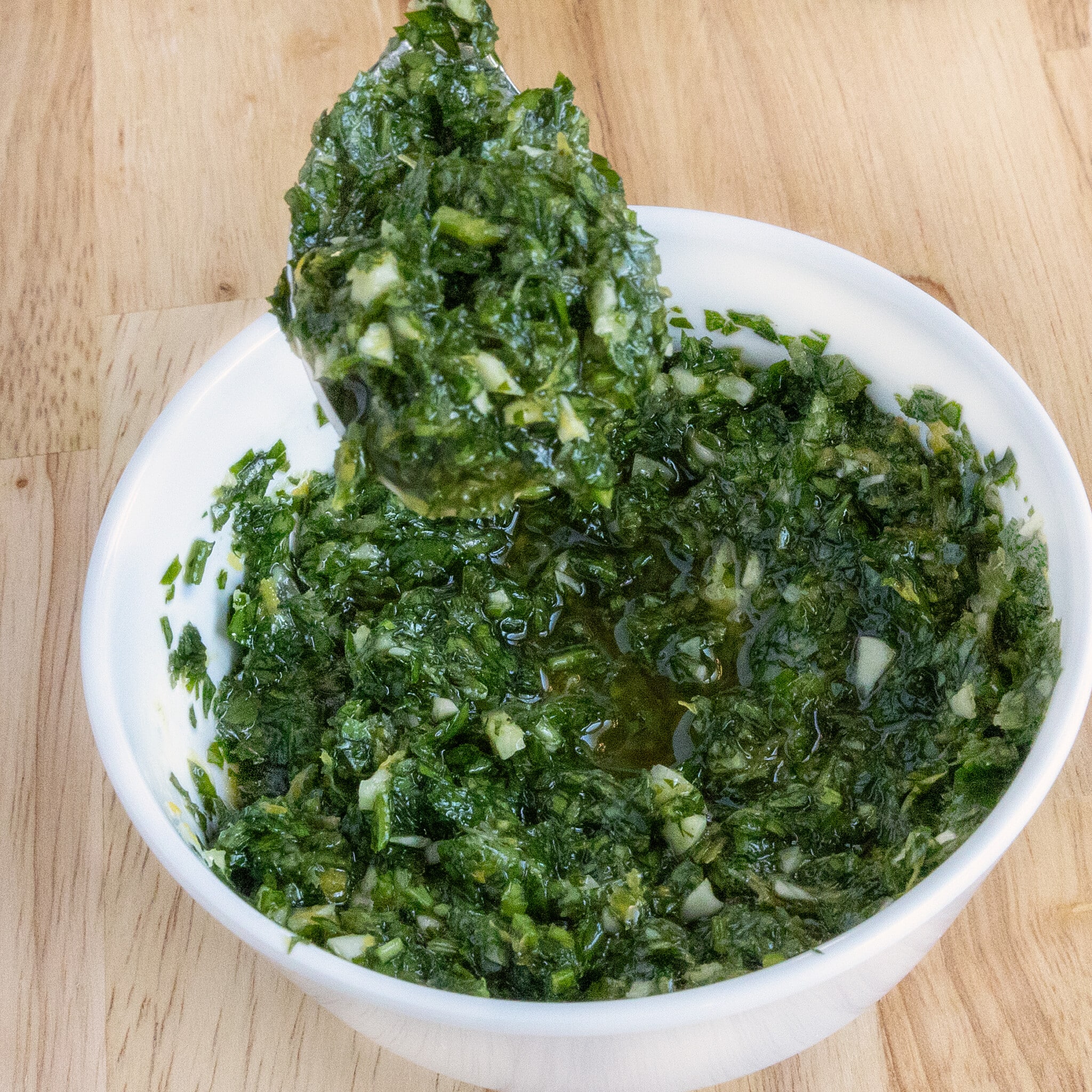 Gremolata in a white bowl with a spoon coming out.